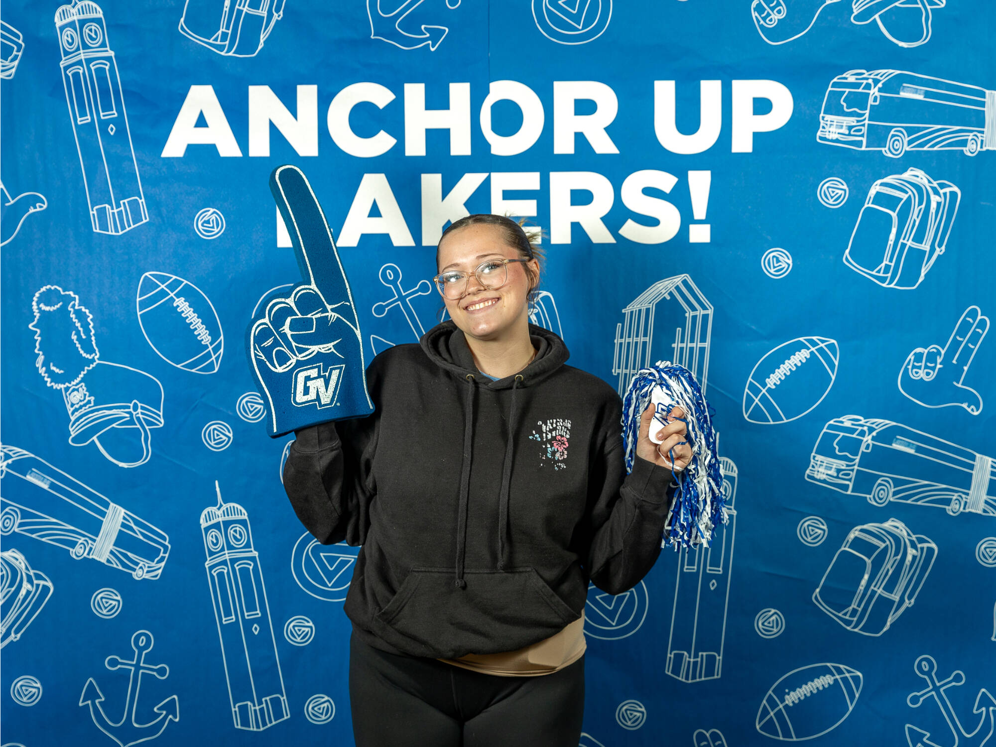 An individual holding up a GVSU foam finger and a blue and white pompom